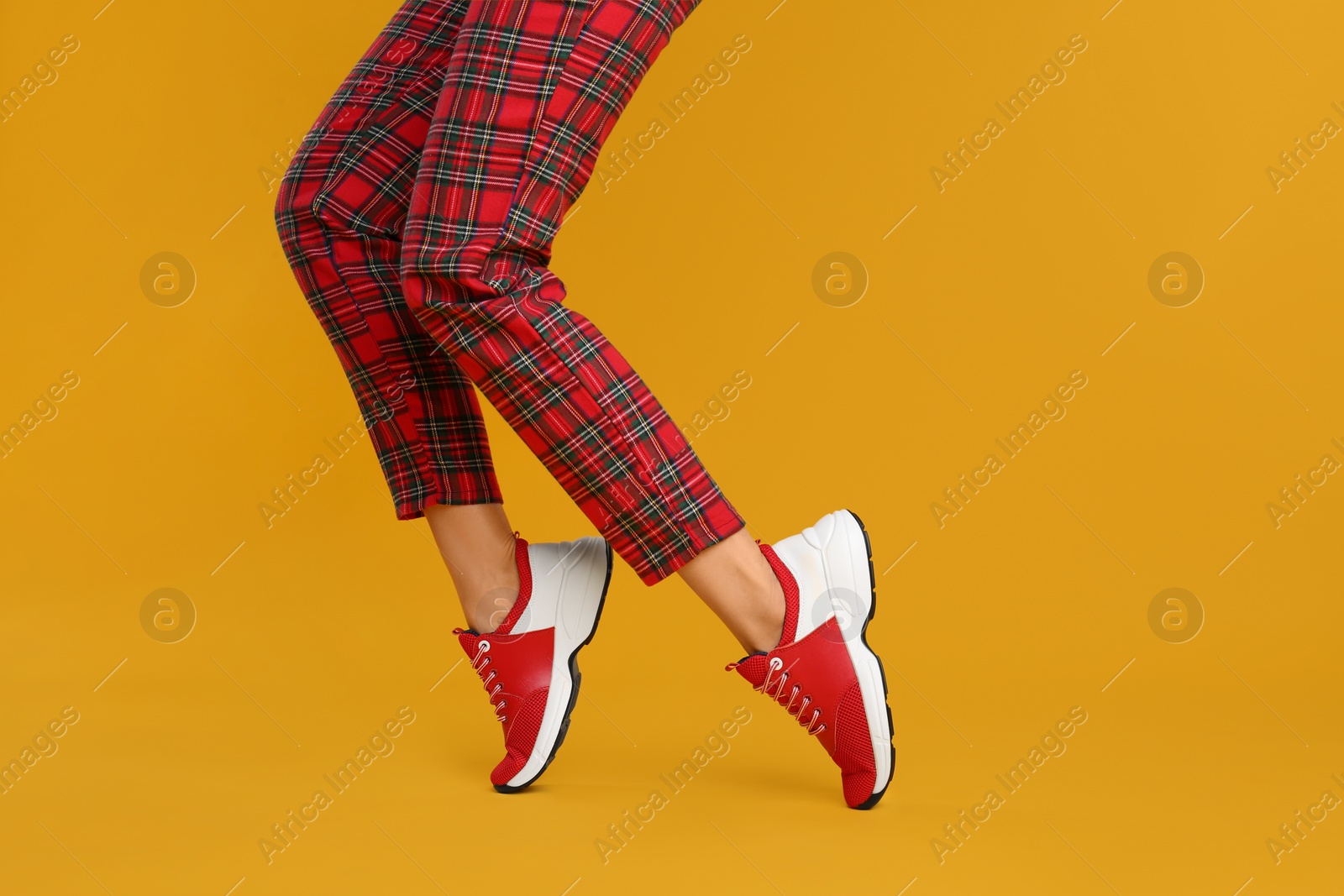 Photo of Woman wearing stylish sneakers on yellow background, closeup