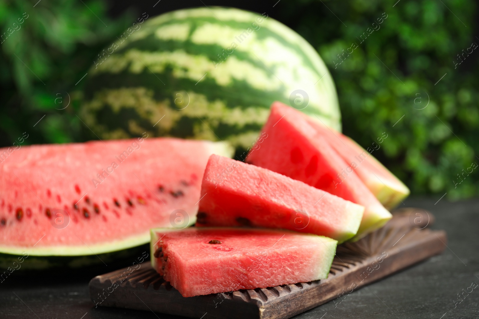 Photo of Whole and cut ripe watermelons on black table