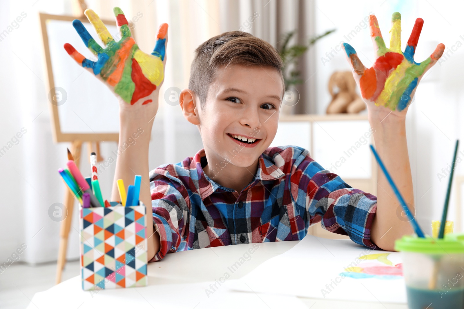 Photo of Little child with painted hands at table indoors