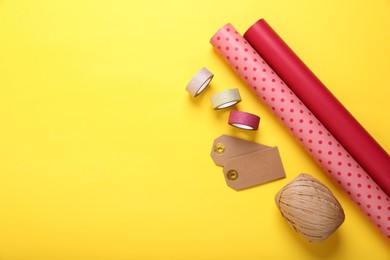 Photo of Rolls of colorful wrapping papers, ribbons and tags on yellow background, flat lay. Space for text