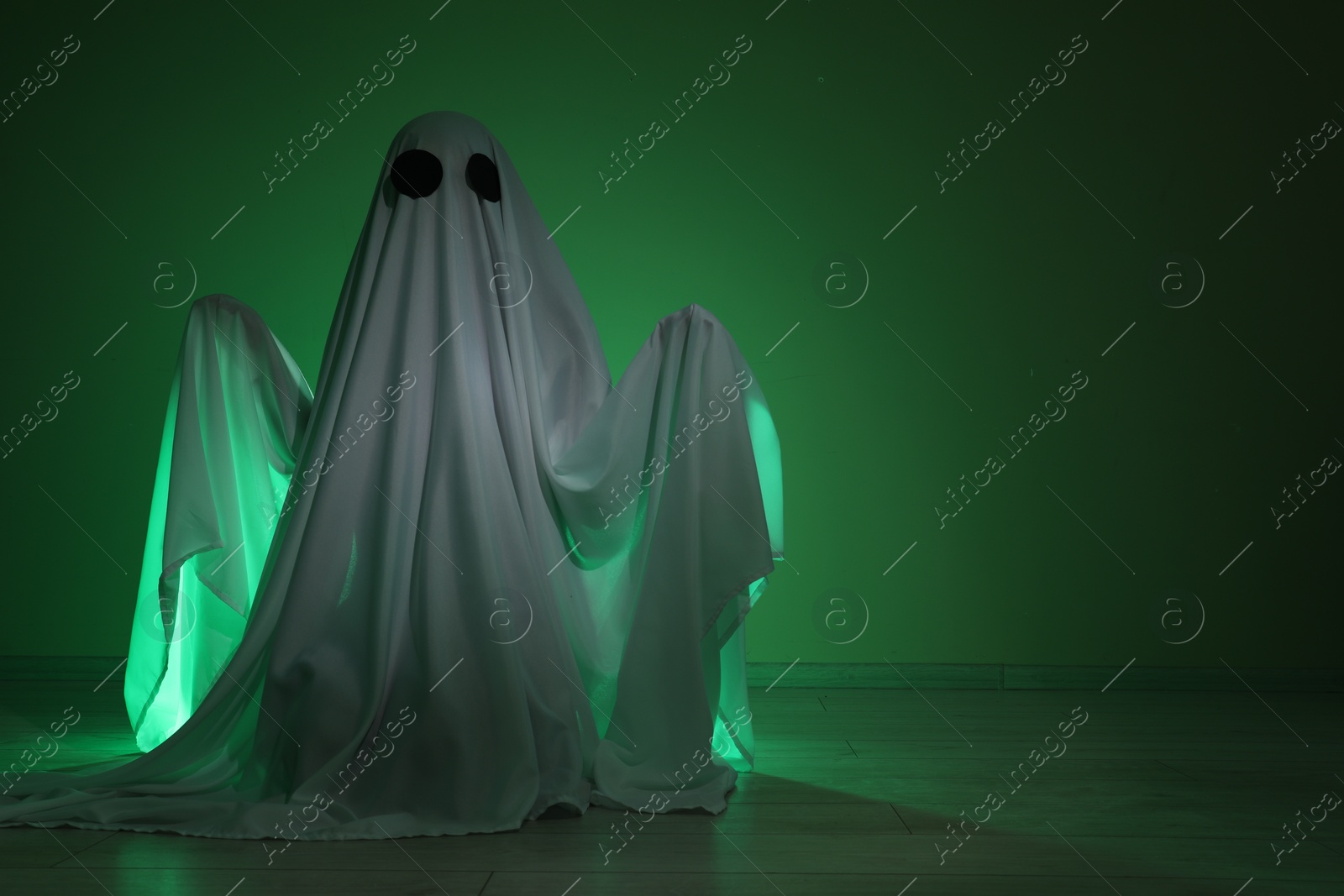 Photo of Creepy ghost. Woman covered with sheet in green light, space for text