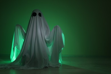 Creepy ghost. Woman covered with sheet in green light, space for text