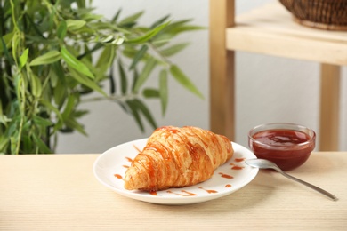 Photo of Plate of fresh croissant served with jam on wooden table indoors, space for text. French pastry