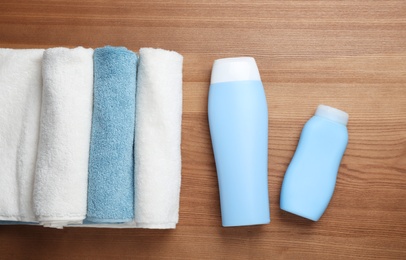 Bottles of shampoo and rolled towels on wooden background, top view