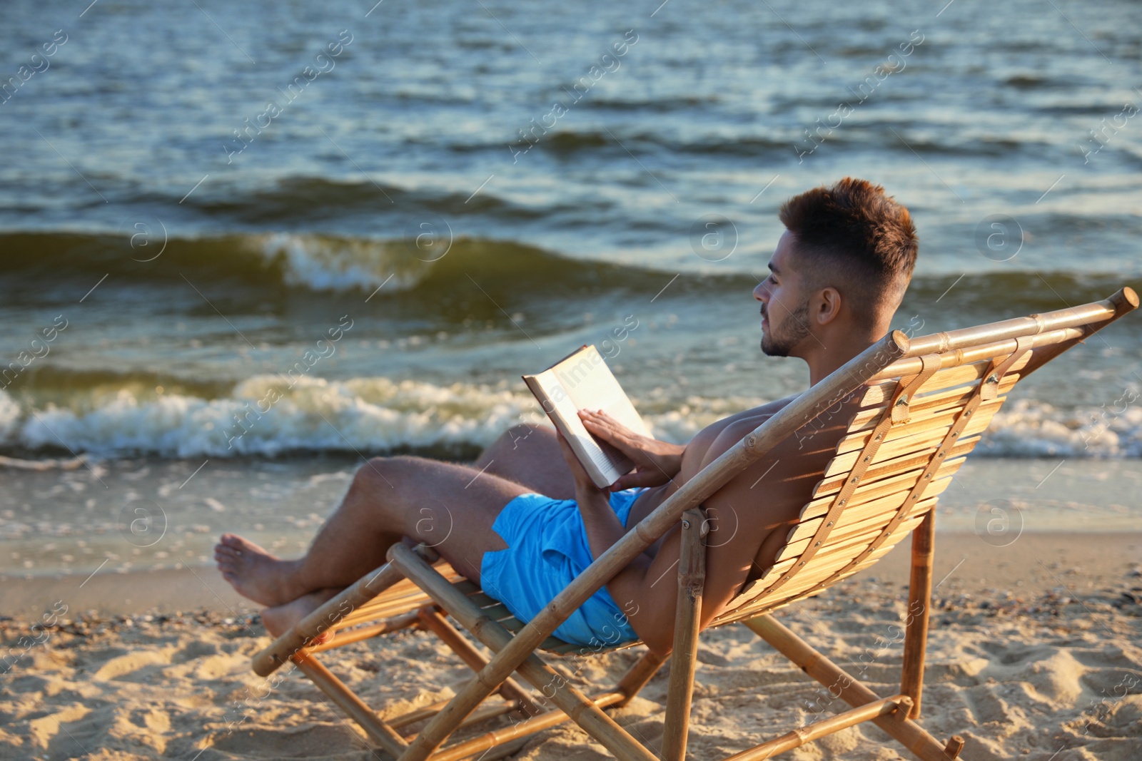 Photo of Young man reading book on sandy beach near sea