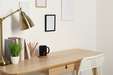 Photo of Comfortable workplace with wooden desk near white wall indoors