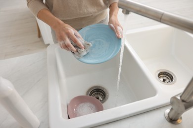 Photo of Woman washing plate above sink in modern kitchen, closeup