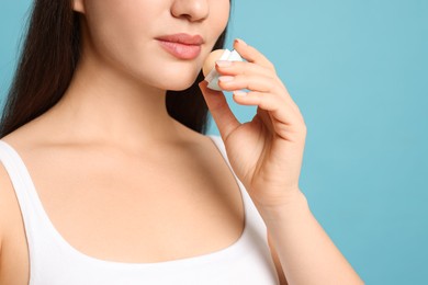 Photo of Young woman applying lip balm on turquoise background, closeup