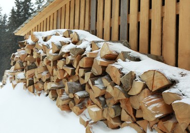 Photo of Many stacked firewood near fence in winter
