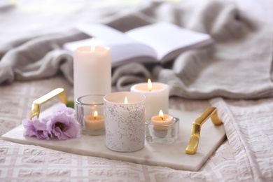 Beautiful burning candles and book on bed at home