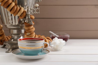 Photo of Cup of tea and delicious ring shaped Sushki (dry bagels) on white wooden table, space for text