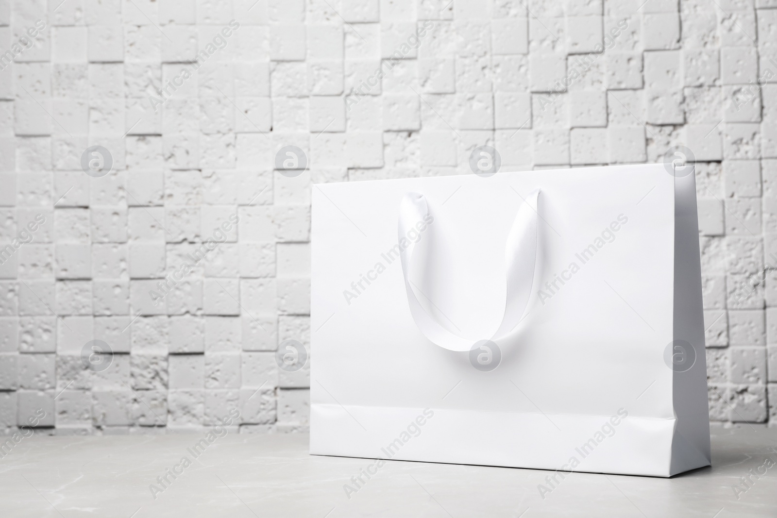 Photo of Paper shopping bag with ribbon handles on table near white wall. Mockup for design