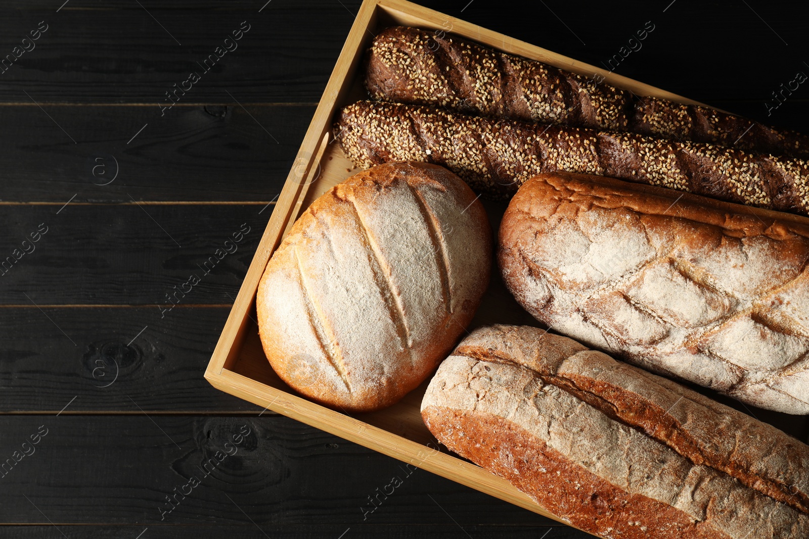 Photo of Basket with different types of fresh bread on black wooden table, top view. Space for text