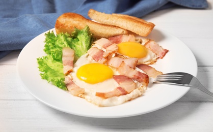Photo of Fried eggs with bacon and toasted bread on plate served for breakfast