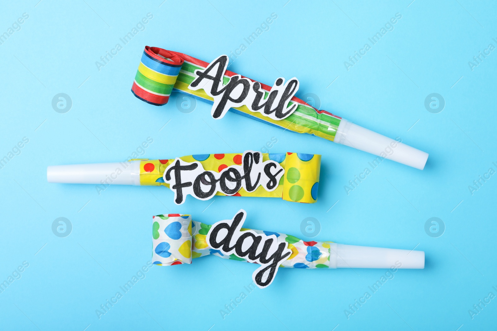 Photo of Party horns with words APRIL FOOL'S DAY on light blue background, flat lay