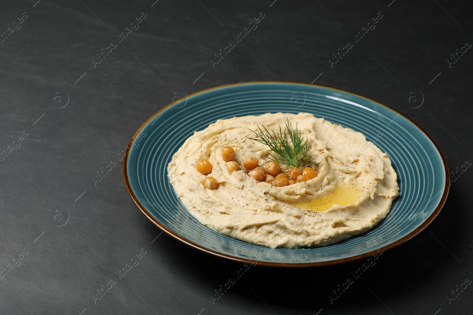 Photo of Plate of tasty hummus with garnish on black table