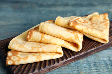 Photo of Fresh thin pancakes on blue wooden table, closeup