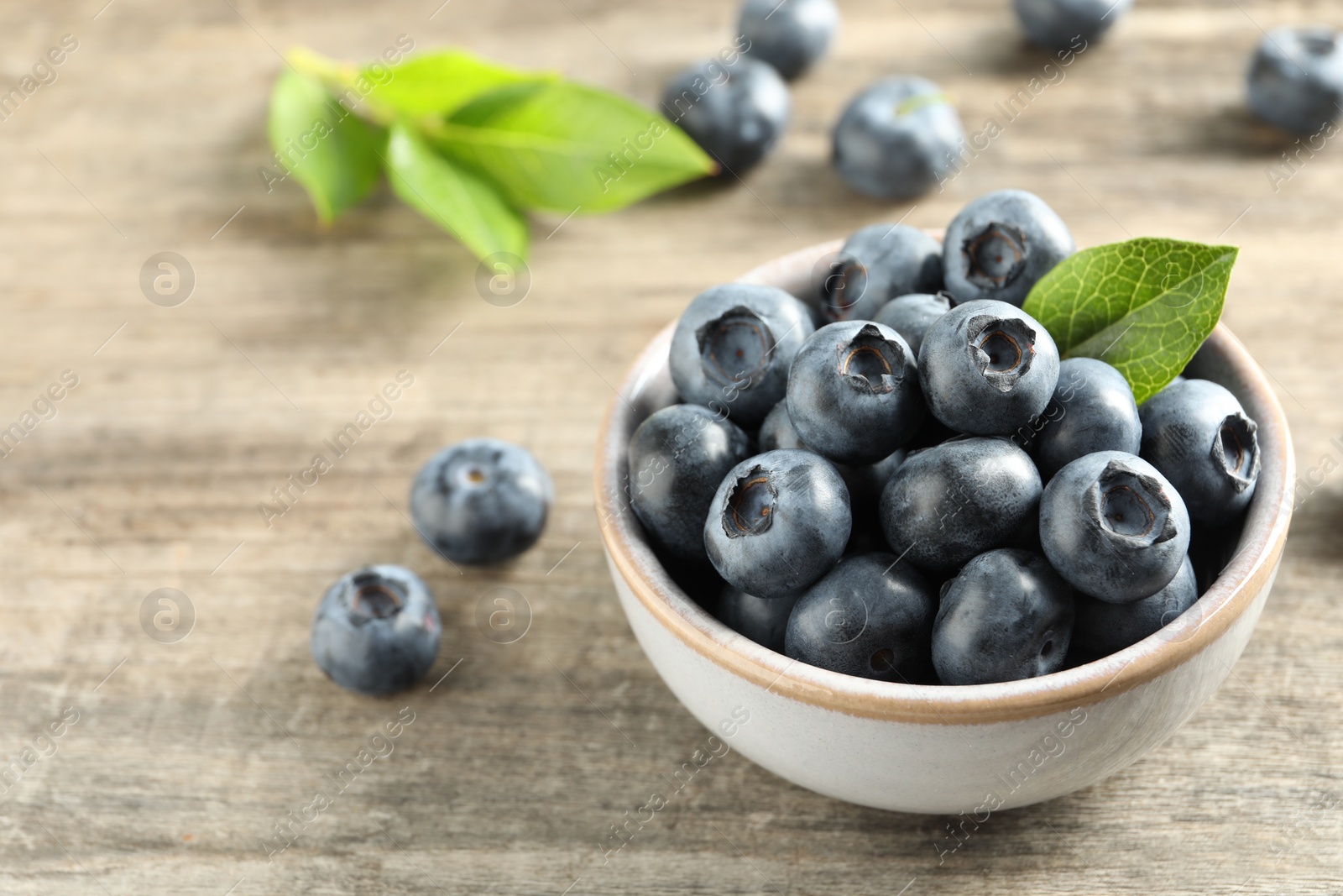 Photo of Bowl of fresh tasty blueberries on wooden table, closeup. Space for text