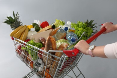 Photo of Woman with shopping cart full of groceries on grey background, closeup