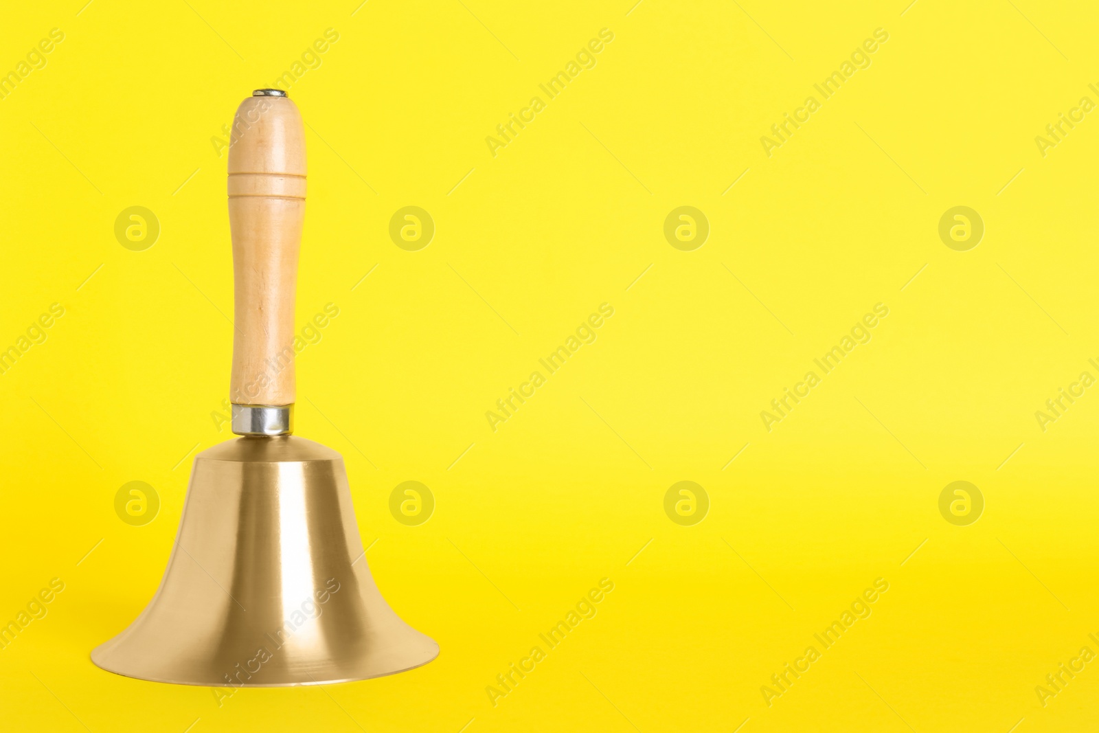 Photo of Golden school bell with wooden handle on yellow background. Space for text