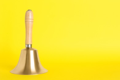 Golden school bell with wooden handle on yellow background. Space for text