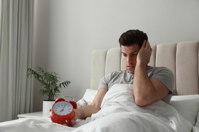 Photo of Emotional man with alarm clock in bed. Being late because of oversleeping