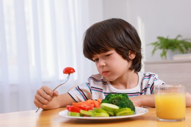 Photo of Cute little boy refusing to eat vegetables at home
