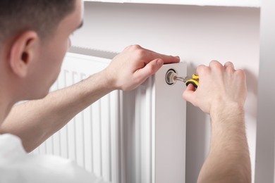 Photo of Professional repairman fixing heating radiator with pliers indoors, closeup