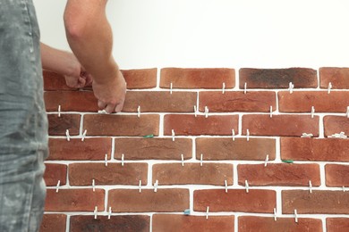 Photo of Professional builder gluing decorative brick on wall, closeup. Tiles installation process