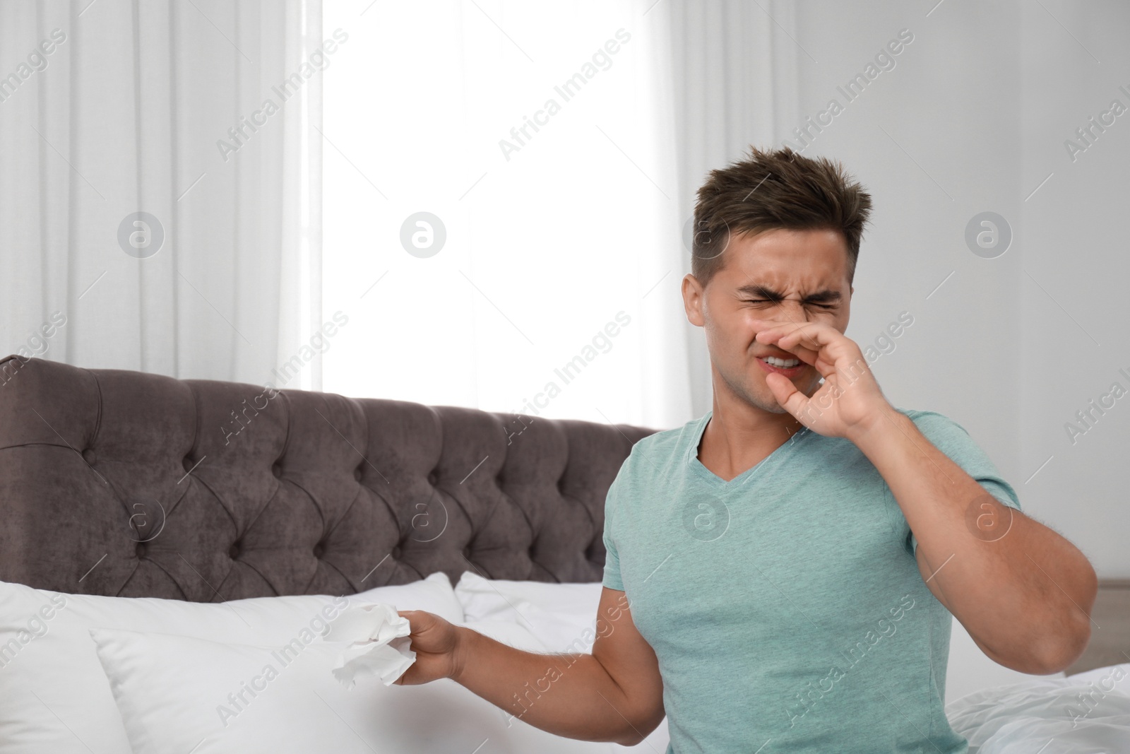 Photo of Young man suffering from allergy in bedroom