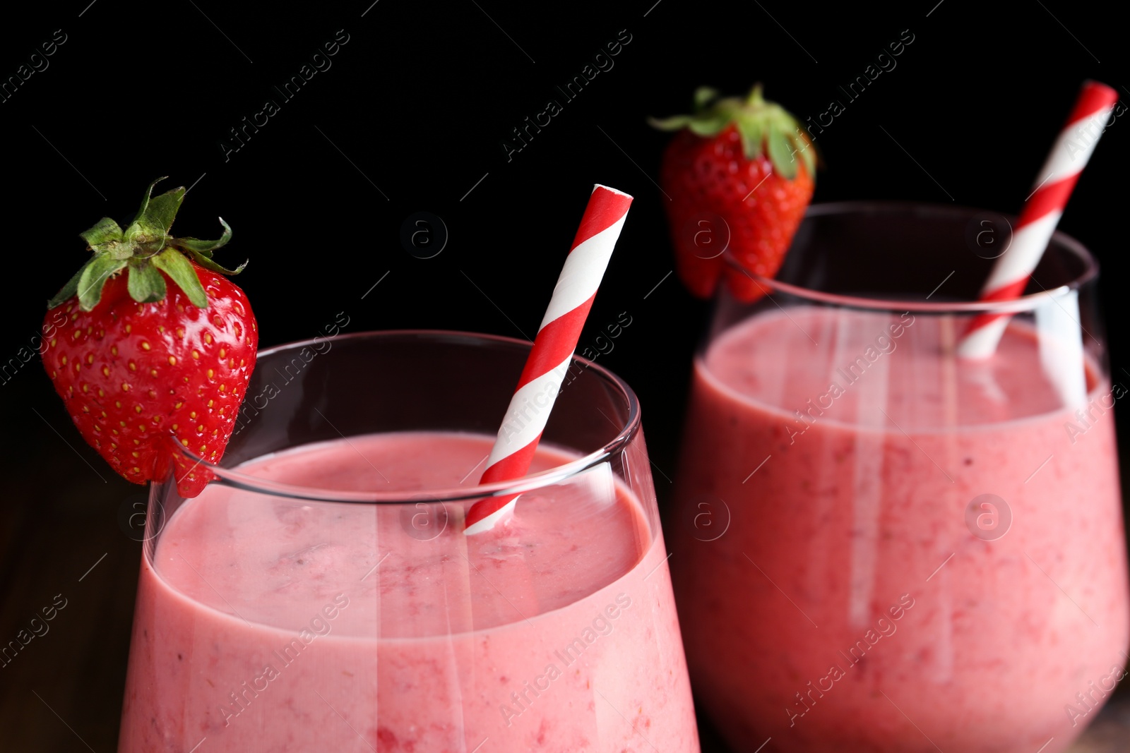 Photo of Tasty strawberry smoothies in glasses on black background, closeup