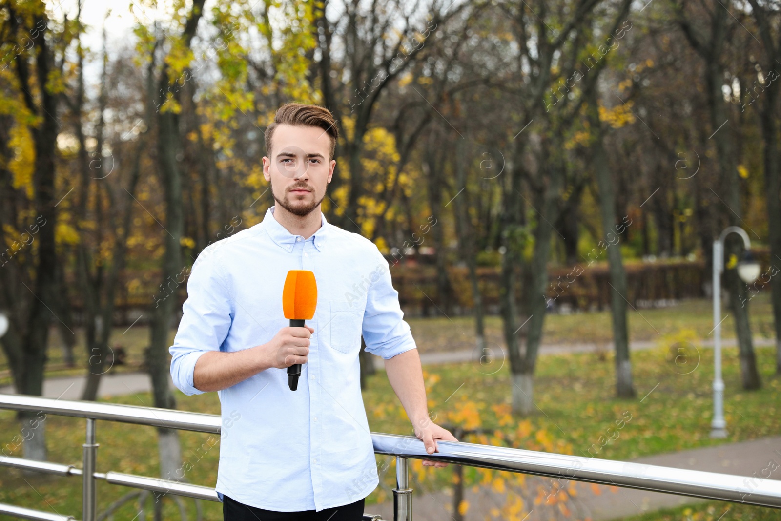 Photo of Young male journalist with microphone working in park