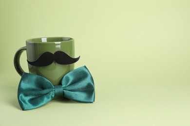 Photo of Man's face made of cup, fake mustache and bow tie on light green background. Space for text
