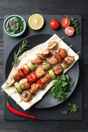 Photo of Delicious shish kebabs with vegetables served on black wooden table, top view