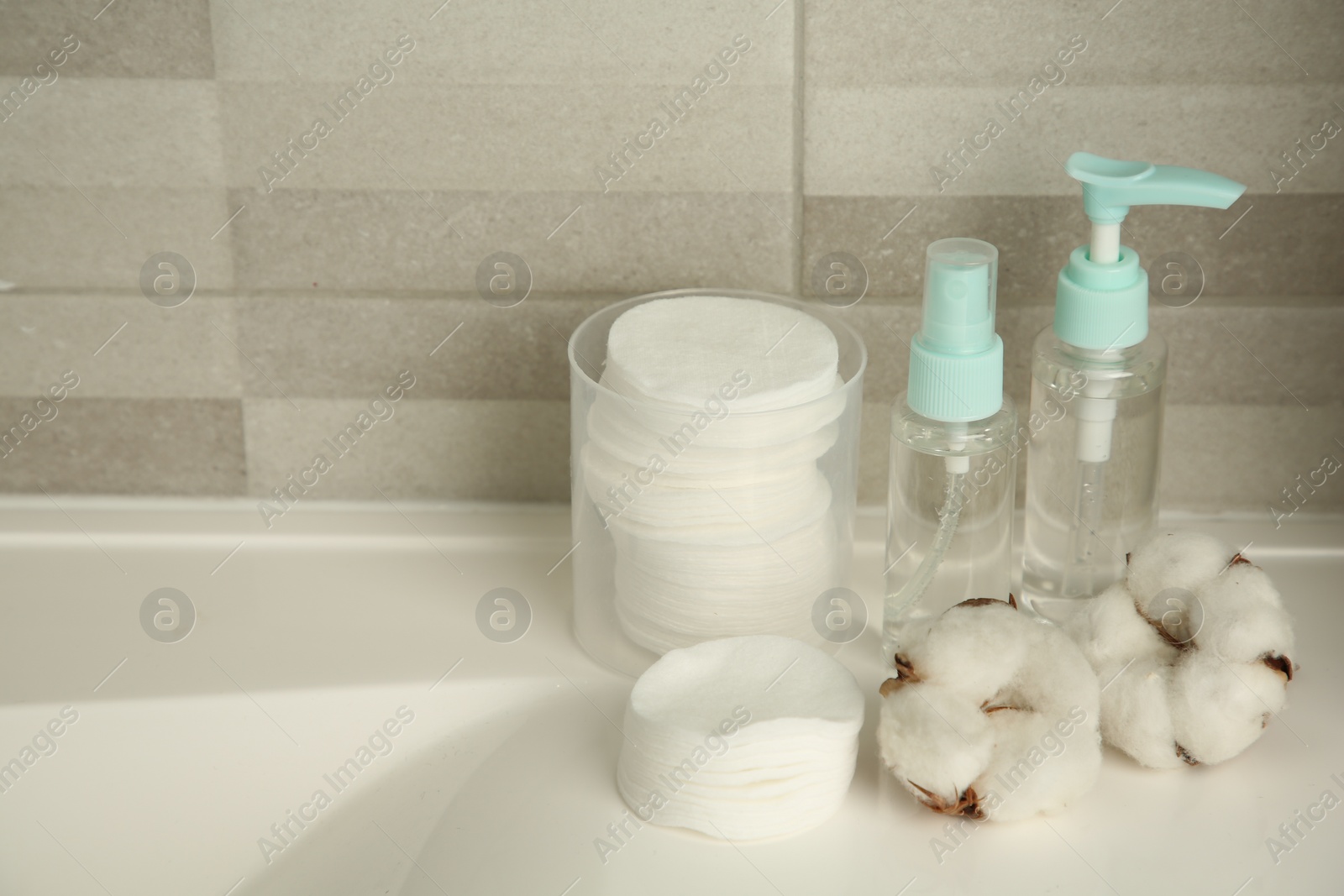 Photo of Cotton pads, cosmetic products and flowers on sink indoors, space for text