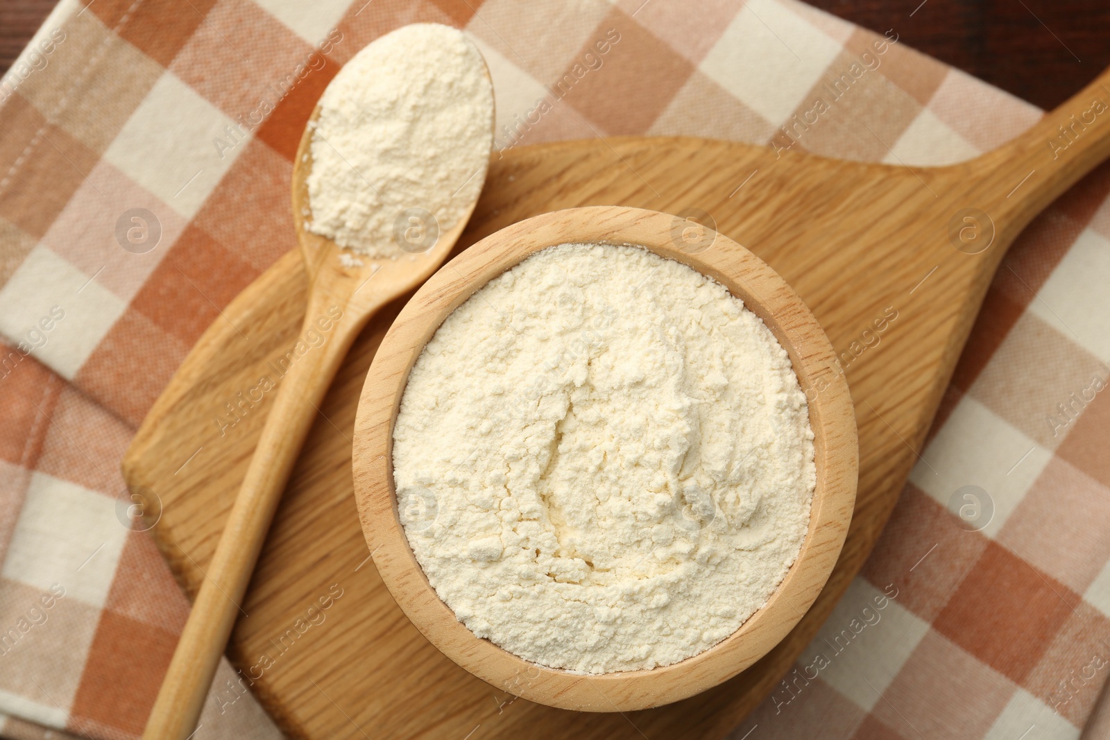 Photo of Baking powder in bowl and spoon on wooden table, top view