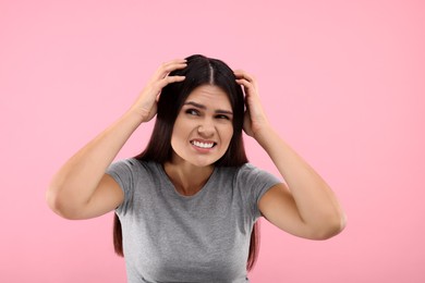 Photo of Emotional woman examining her hair and scalp on pink background. Dandruff problem