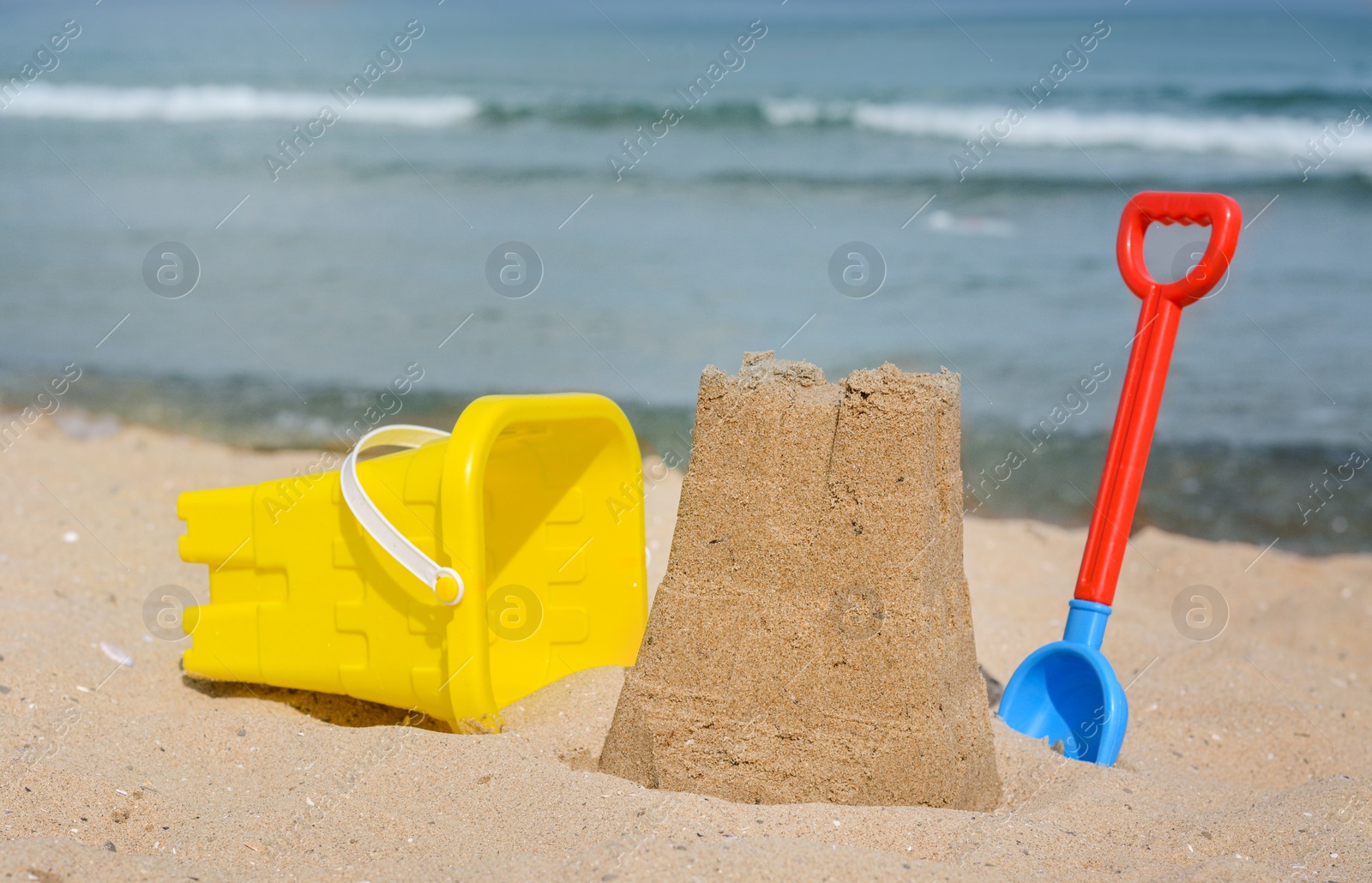 Photo of Beautiful sand castle, child plastic shovel and bucket on beach near sea