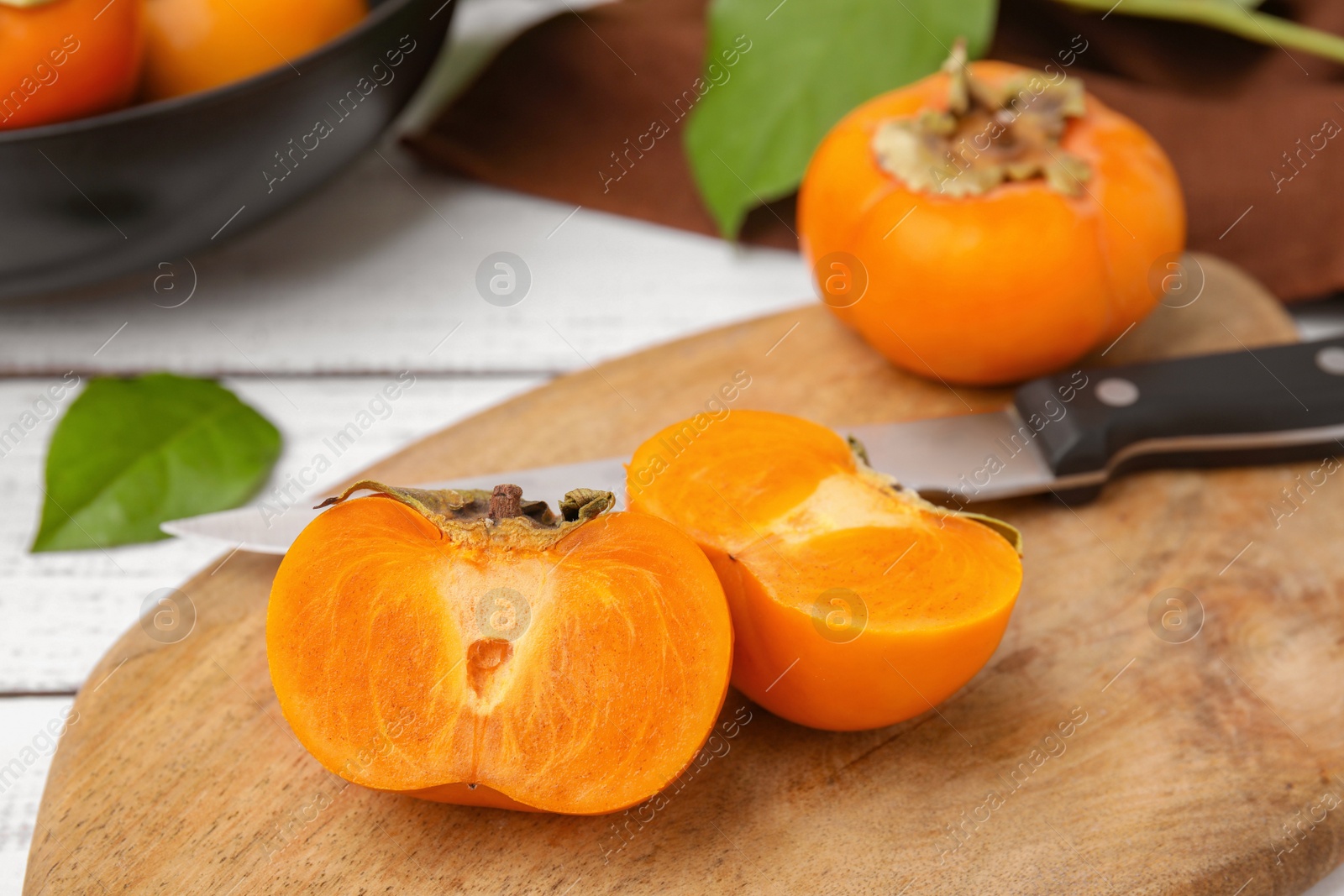 Photo of Whole and cut delicious ripe persimmons on white wooden table