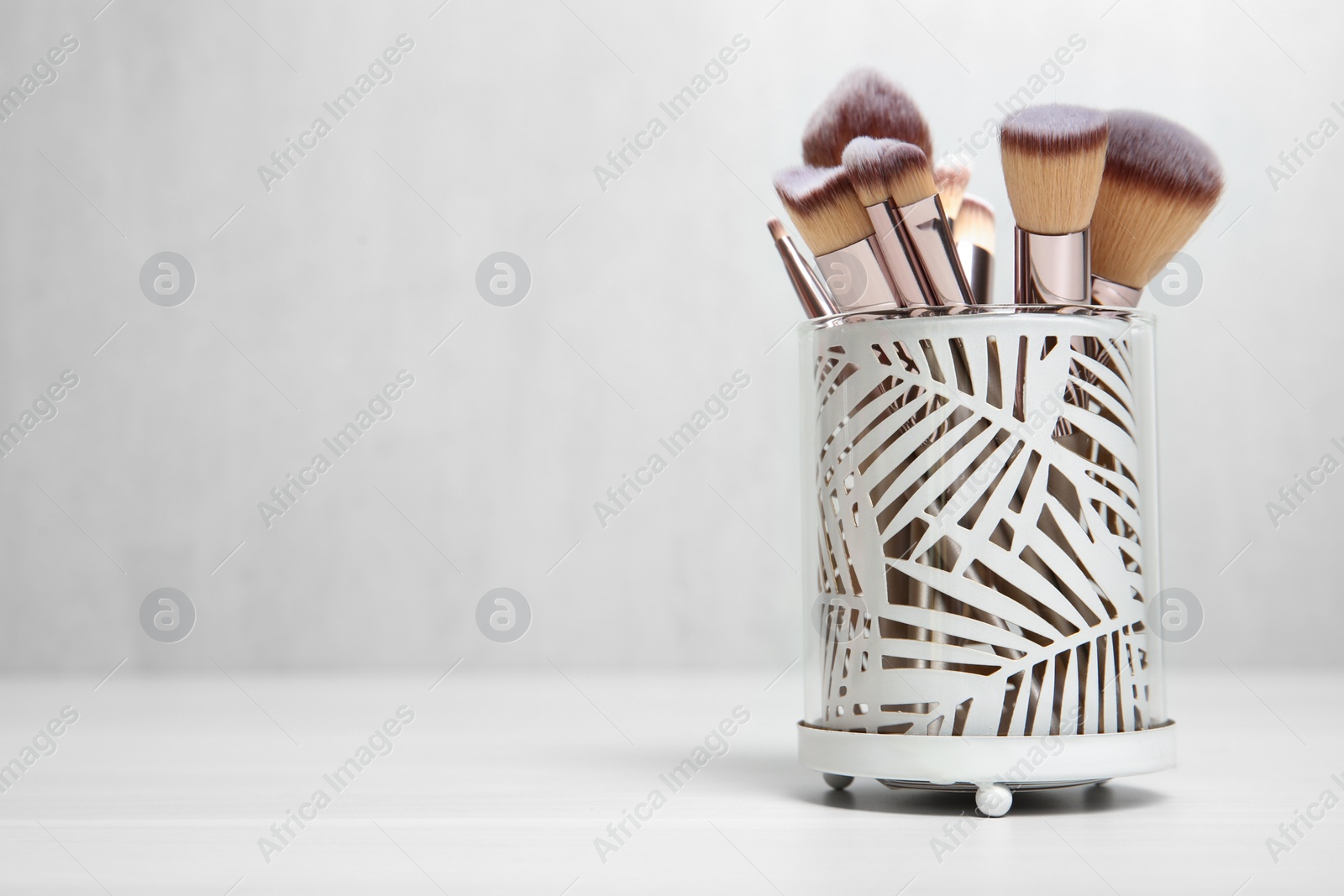Photo of Organizer with professional makeup brushes on light table. Space for text