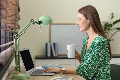 Young woman with cup of coffee working on laptop at home