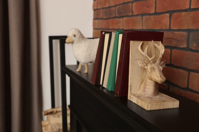 Photo of Bookends with books on fireplace near red brick wall indoors, space for text