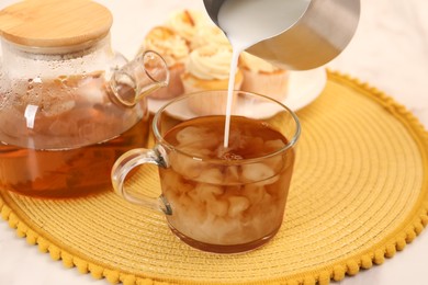 Photo of Pouring milk in tea at table, closeup