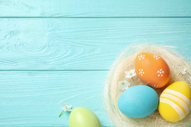 Photo of Colorful Easter eggs in decorative nest and flowers on light blue wooden background, flat lay. Space for text