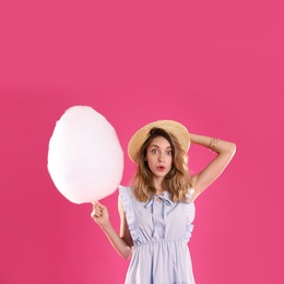 Emotional young woman with cotton candy on pink background