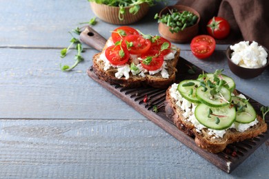 Delicious sandwiches with vegetables, cheese and microgreens on grey wooden table. Space for text