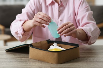 Photo of Woman packing cosmetic travel kit into compact toiletry bag at wooden table indoors, closeup. Bath accessories