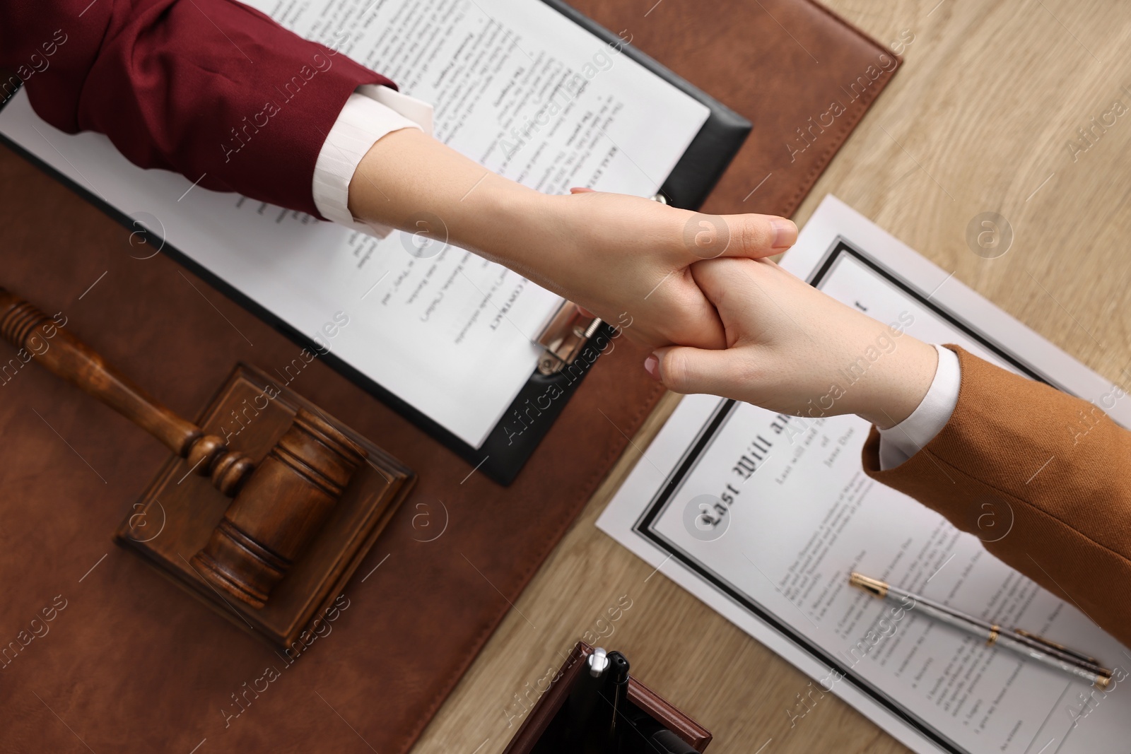 Photo of Notary shaking hands with client at wooden table, top view