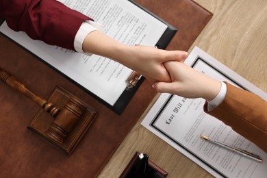 Photo of Notary shaking hands with client at wooden table, top view