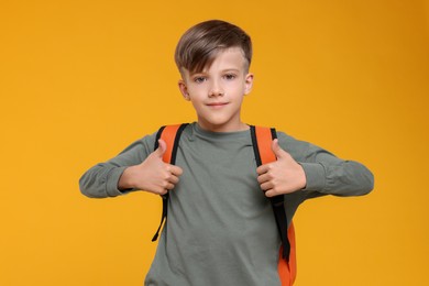 Photo of Cute schoolboy showing thumbs up on orange background